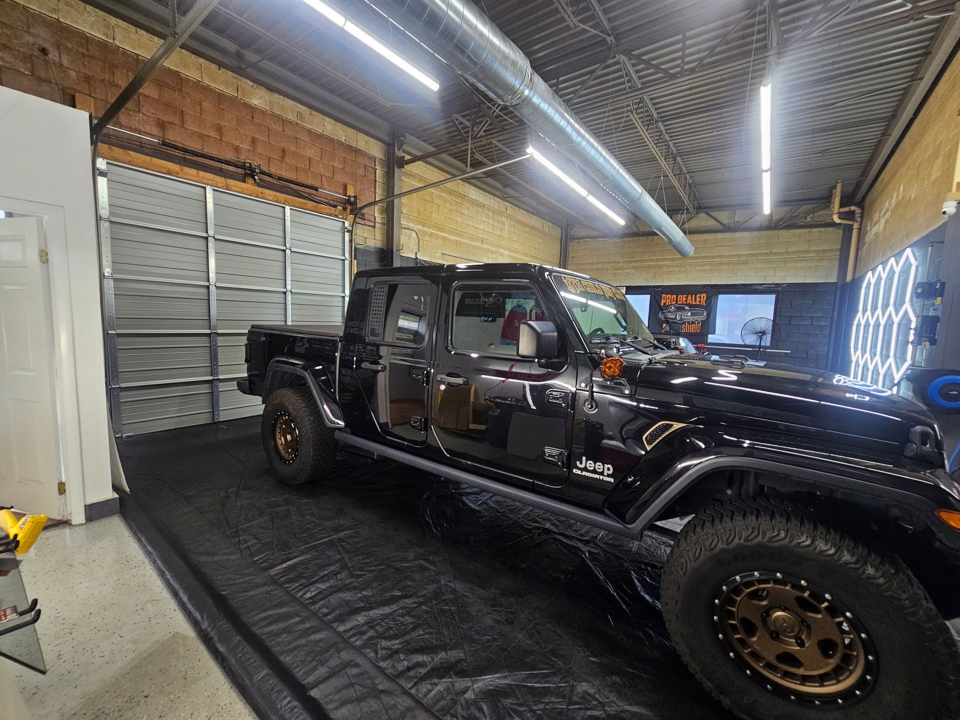 Black Jeep pickup truck inside a garage with lighting and equipment.
