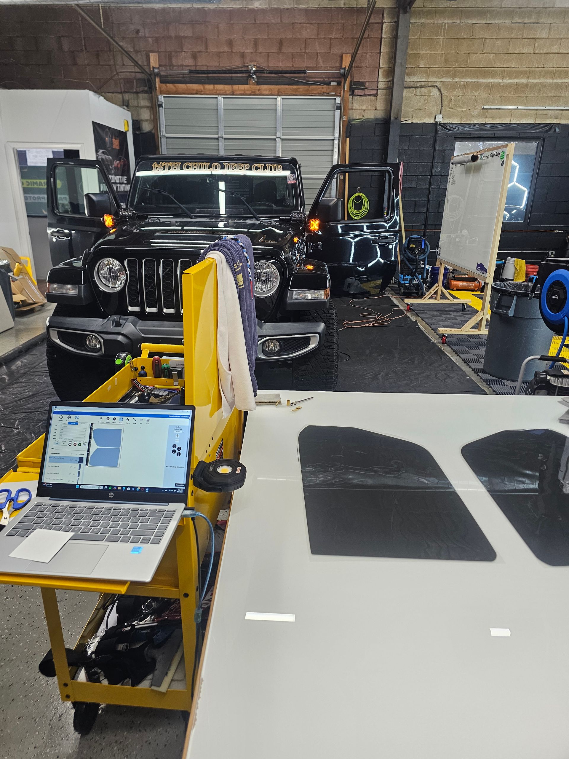Black Jeep in a shop, laptop on cart, working on panels.