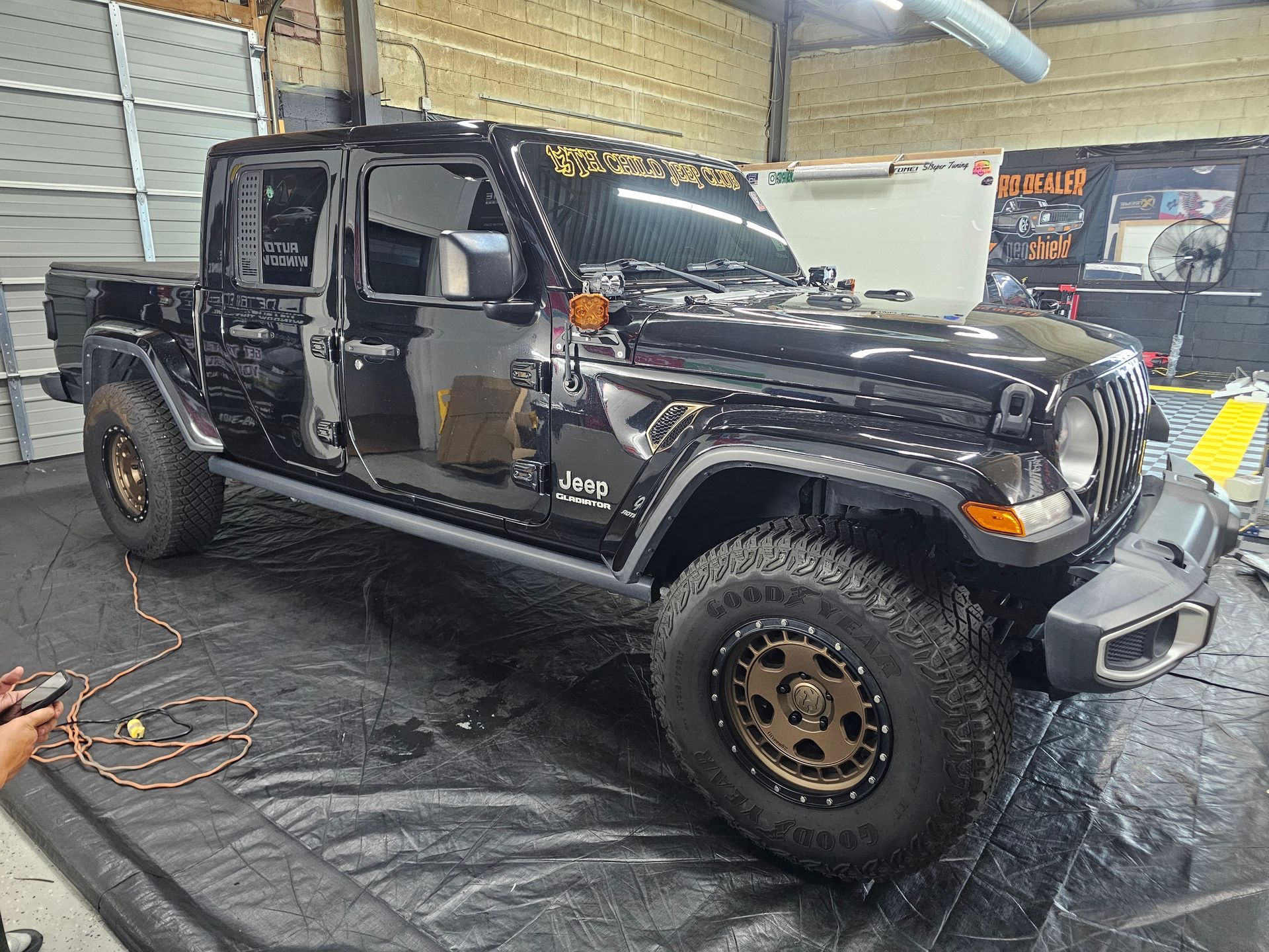 Black Jeep Gladiator truck with bronze wheels in a workshop setting.
