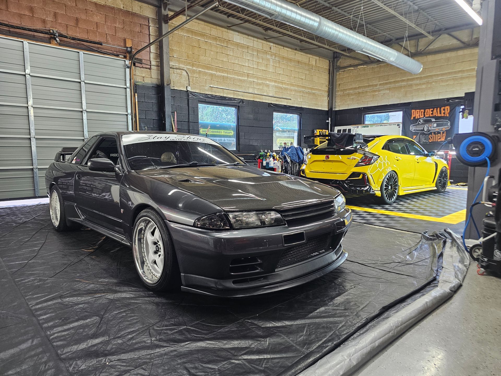 Dark gray Nissan Skyline R32 and yellow Honda Civic Type R in a garage.
