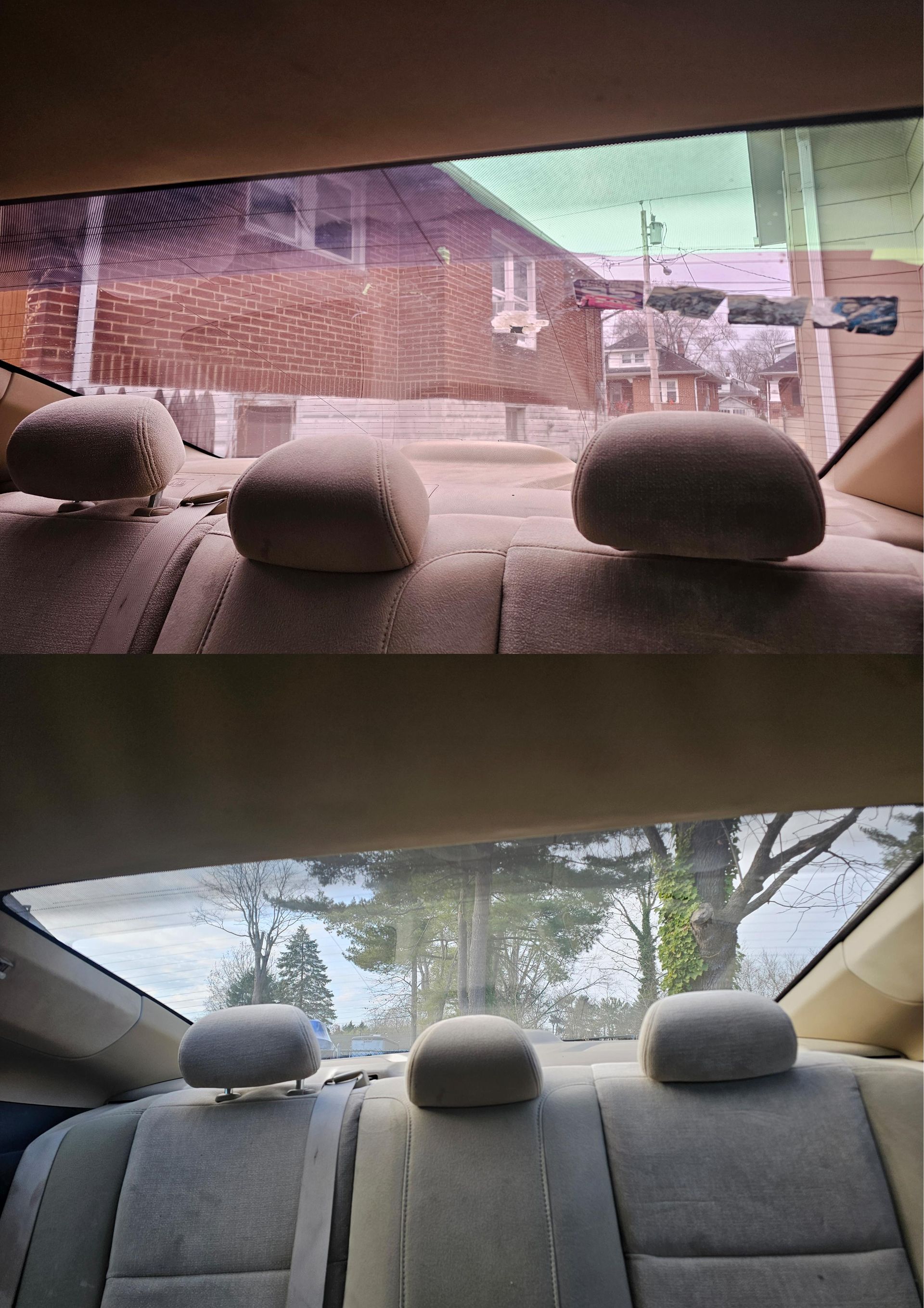 View from inside a car looking out the back window at a building and trees. Beige seats are visible.