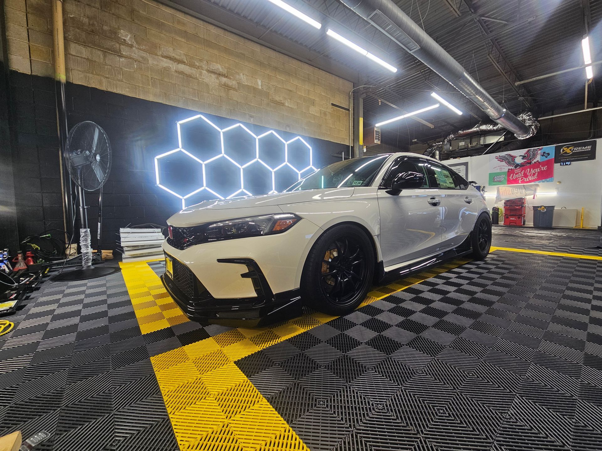 White Honda Civic in a garage with black and yellow flooring, neon honeycomb lights.