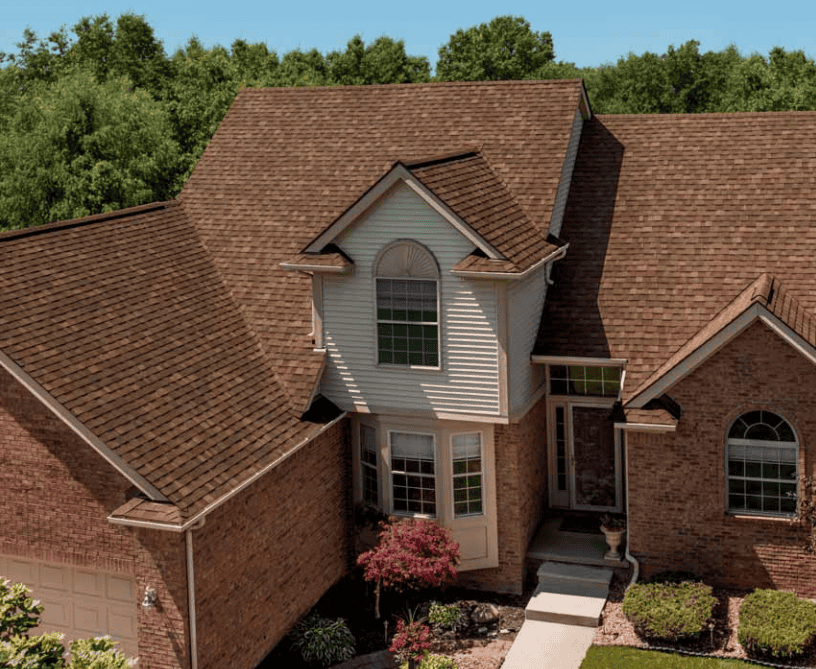 Aerial view of a brick suburban house with a brown shingle roof and front walkway