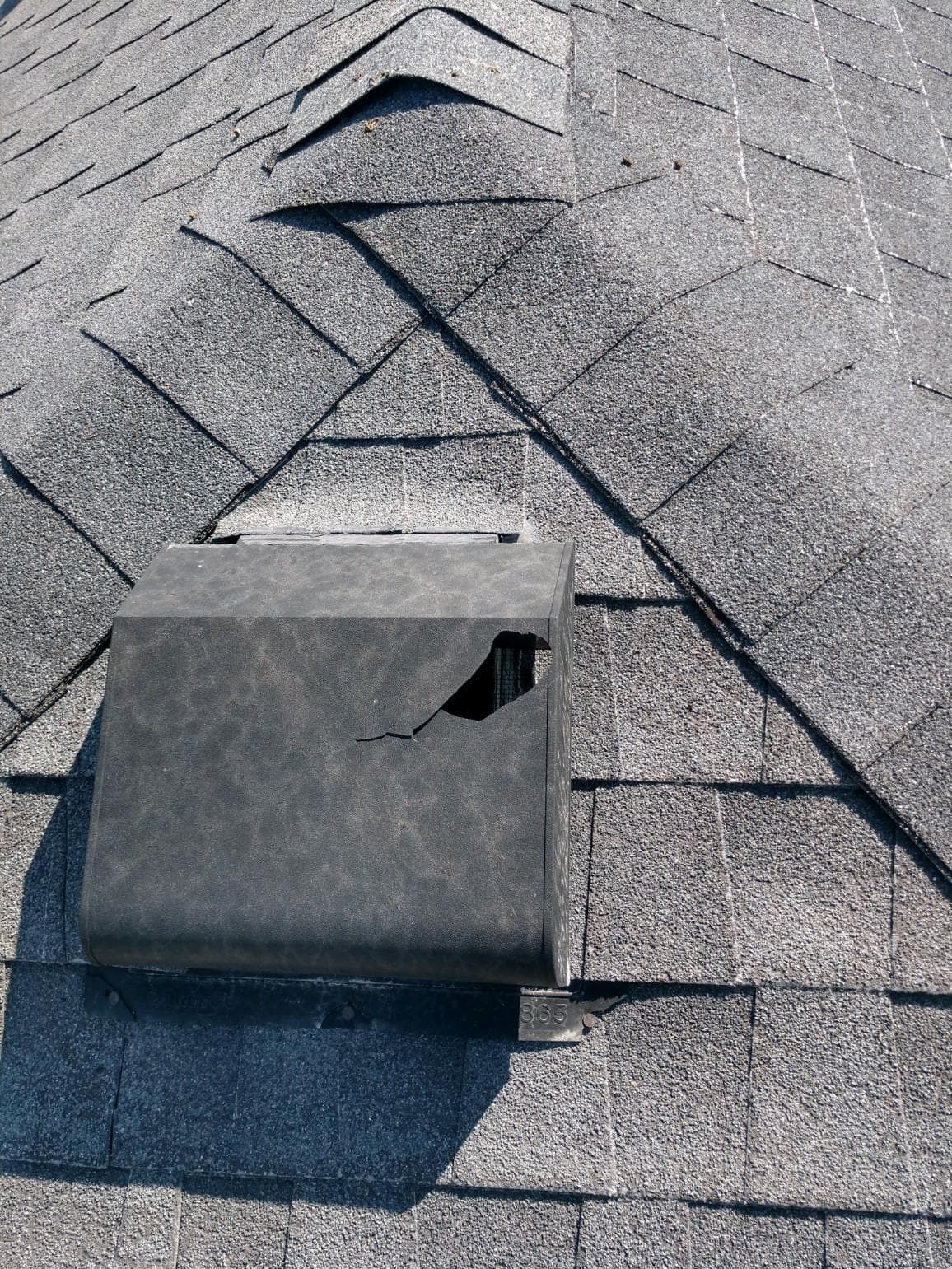 Roof vent cap on gray shingle roof with visible damage and a bent side panel