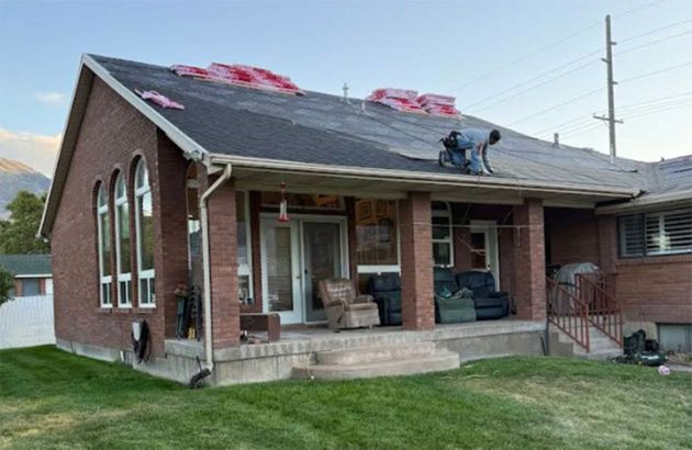 Brick house with damaged roof and porch, seen in a residential yard.