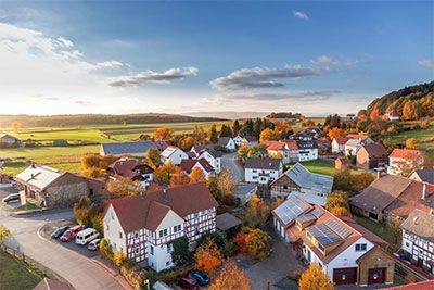 Aerial view of a village with red-roofed houses beside green fields at sunset