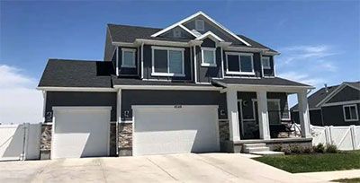 Modern two-story gray house with two white garage doors and a front porch under a clear sky