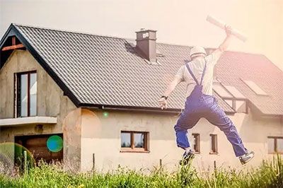 Person jumping in front of a house with a tiled roof and sun flare in the background