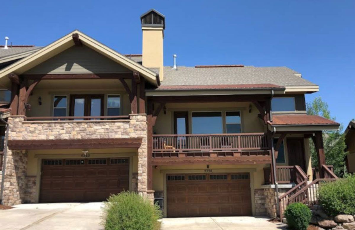 Two-story stone and stucco house with two garage doors, front porch, and chimney under a clear blue sky