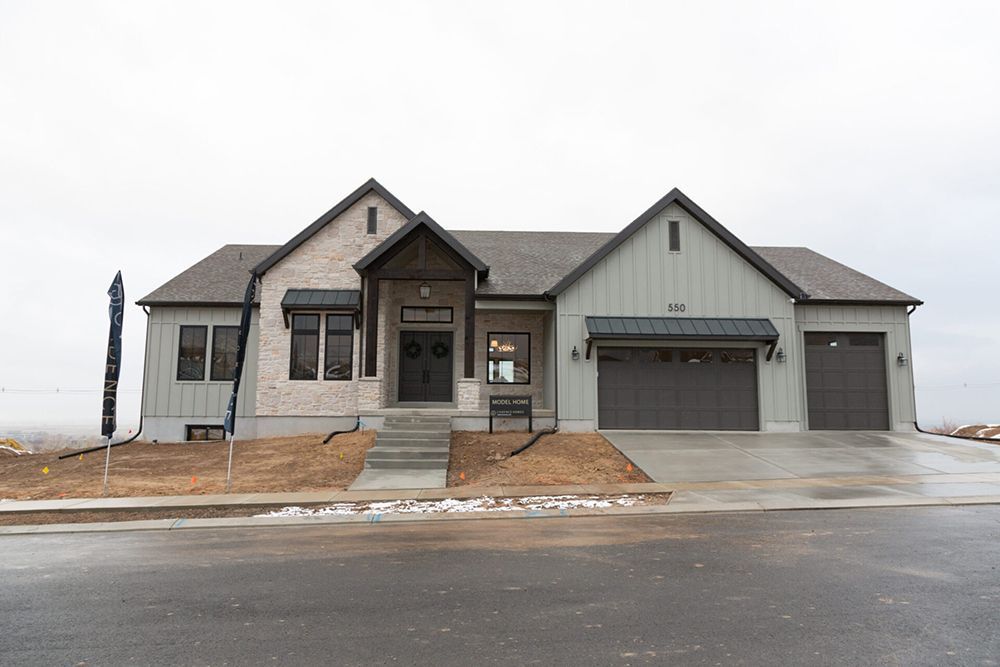 Modern single-story house with gray siding, stone entry, and attached two-car garage on a wet street