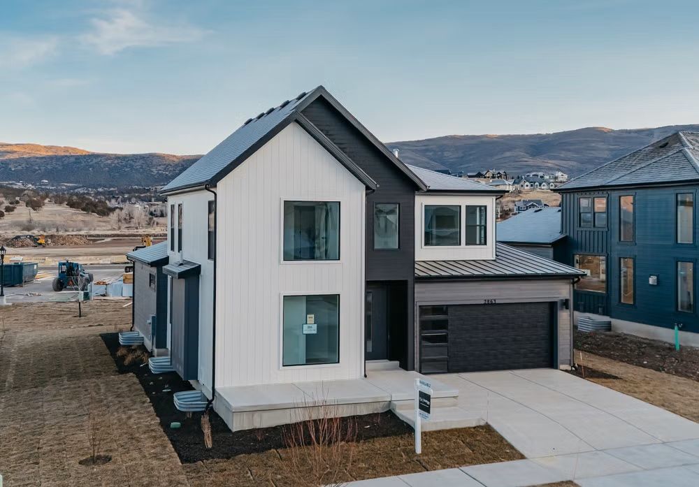 Modern two-story white house with dark trim, attached garage, and mountain backdrop in a new neighborhood