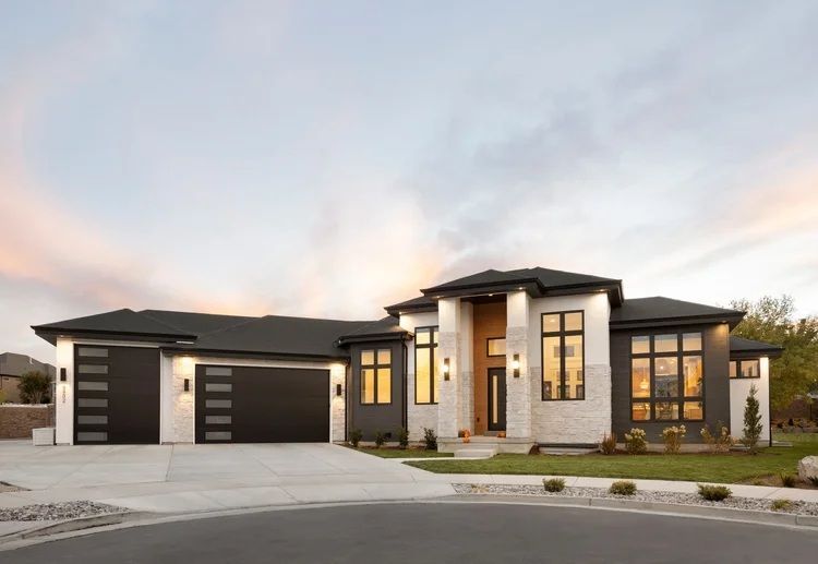Modern single-story house with stone facade, dark roof, and two-car garage at dusk