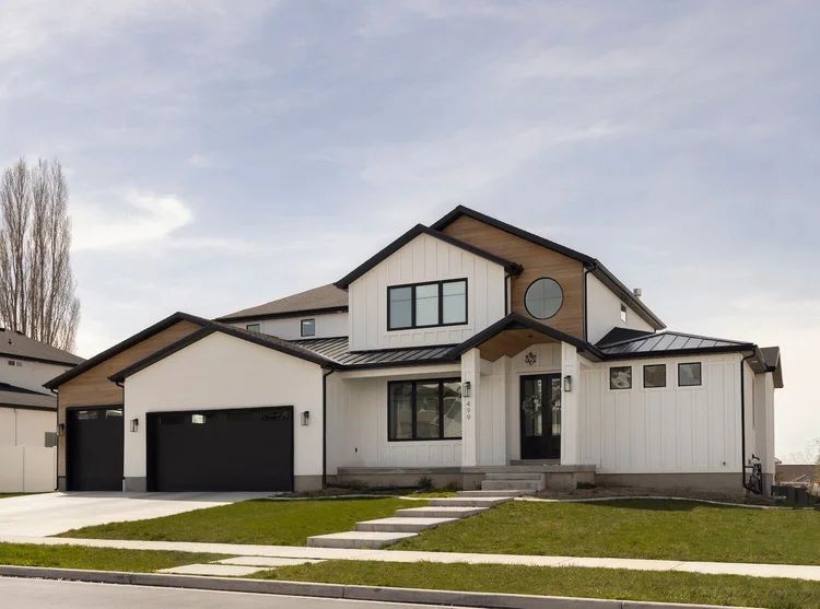 Modern two-story suburban house with white siding, black garage doors, and a small front lawn