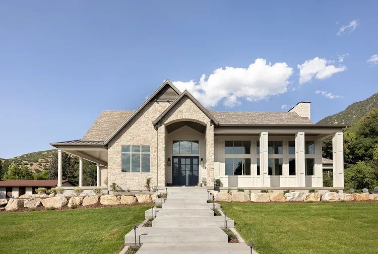 Stone house with front porch, central walkway, and green lawn under a blue sky
