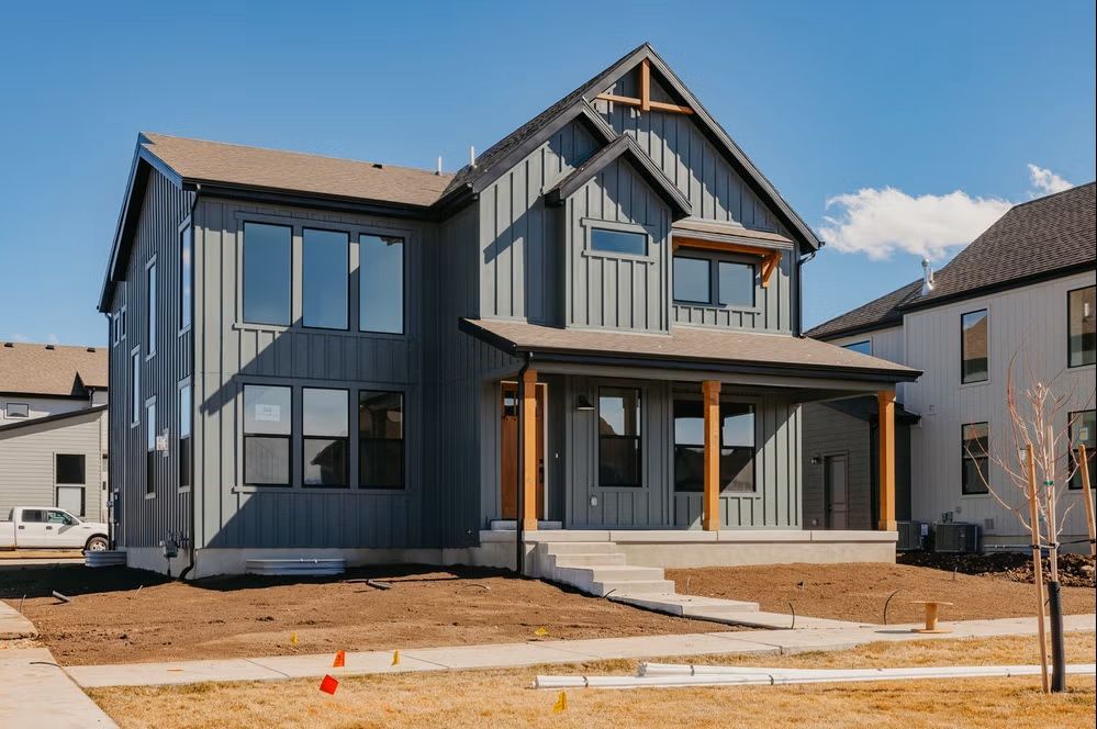 New gray two-story house with front porch and unfinished yard under construction