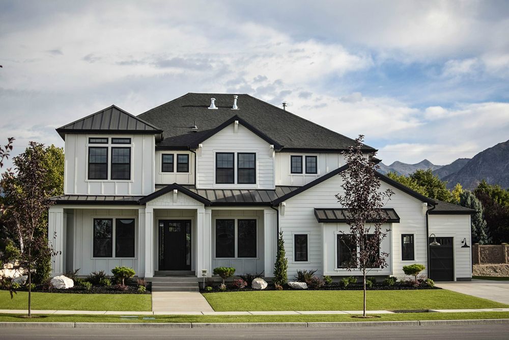 Modern two-story white house with dark roof, front porch, and manicured lawn under cloudy sky