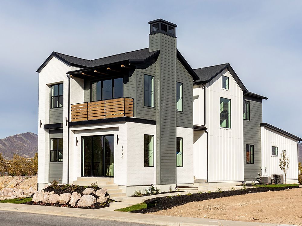 Modern two-story house with gray and white siding, wooden balcony, and stone accents