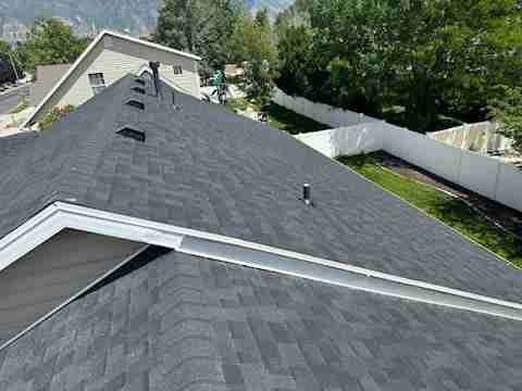 Roof with dark gray shingles and several vents, viewed from above near a residential neighborhood
