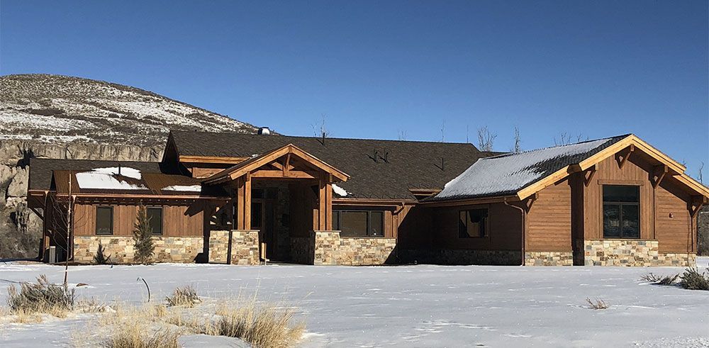 Snow-covered rustic cabin with wooden porches and a mountain backdrop under a clear blue sky