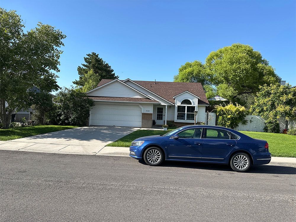 Blue sedan parked in front of a suburban house with a driveway and trees