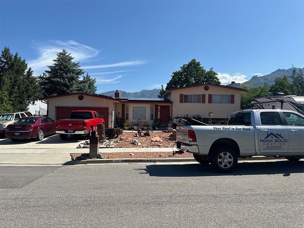 Two pickup trucks parked outside a single-story house under a clear blue sky.