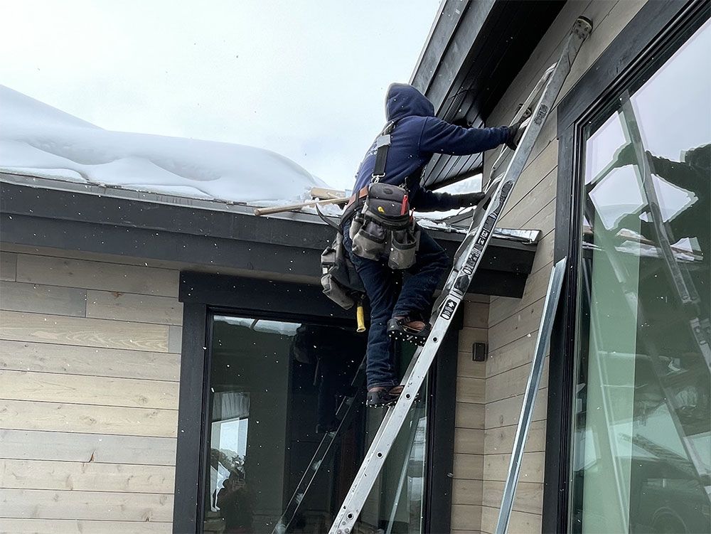 Worker on ladder repairing a roof gutter beside a house in winter.