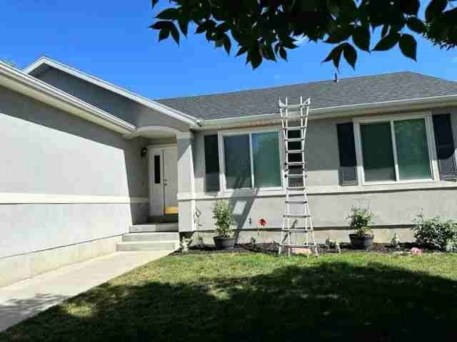 House exterior with a ladder leaning against the roof in a sunny front yard