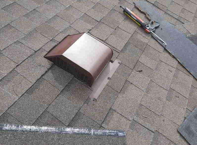 Roof vent on gray shingles with tools lying nearby