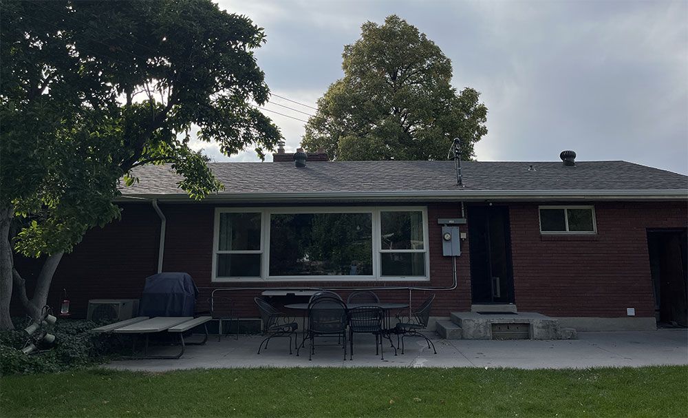 Single-story brick house with a front porch, large window, and two trees in the yard