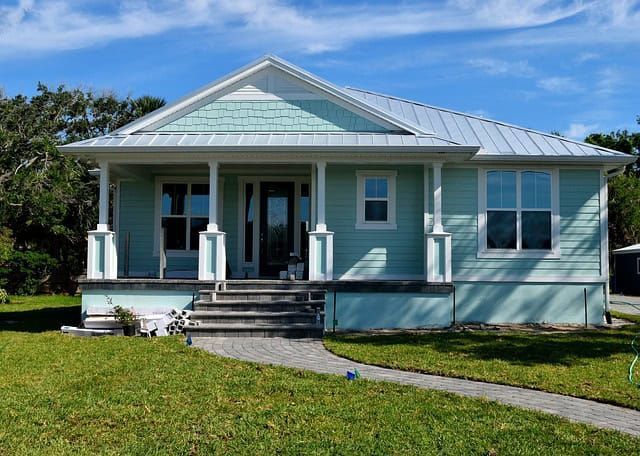 Blue house with white trim, front porch, and steps on a sunny lawn