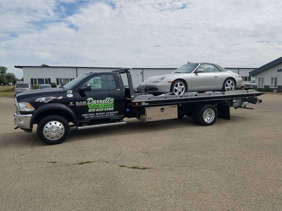 Tow truck hauling a silver Porsche on a sunny day.
