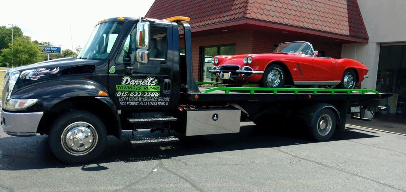 Black tow truck transporting a red convertible on a sunny day.