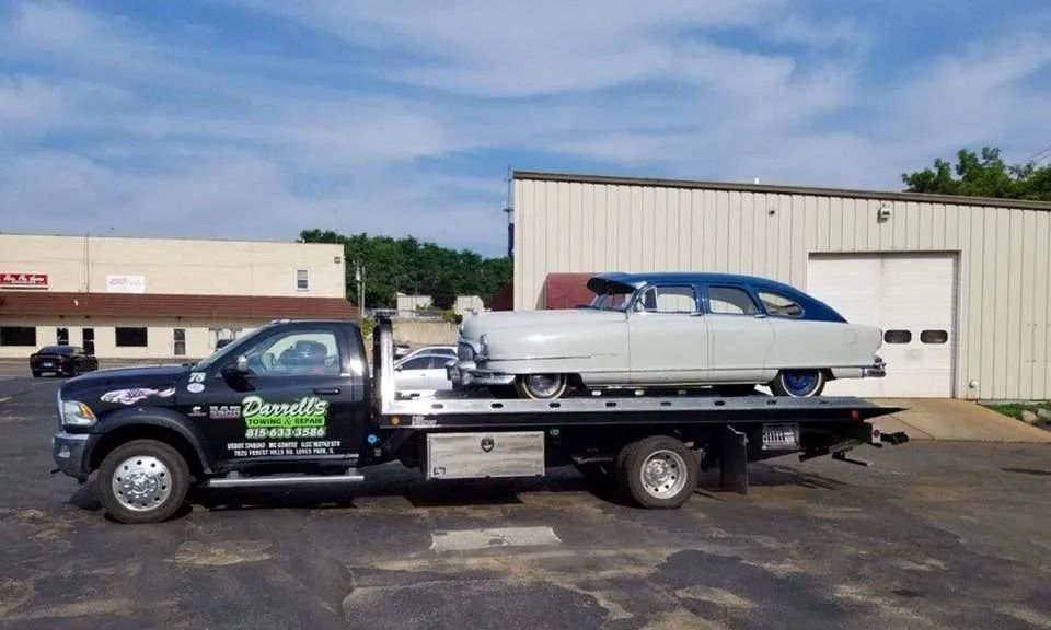 Tow truck carrying a light blue and white classic car on a sunny day.