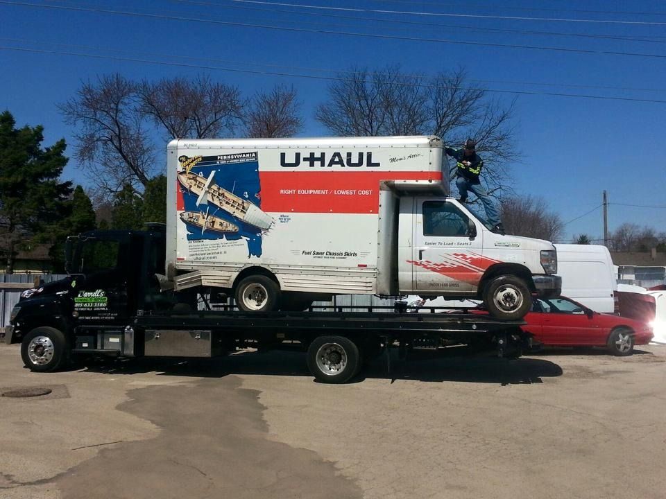 U-Haul box truck being towed on a flatbed tow truck; a person on top of the box.