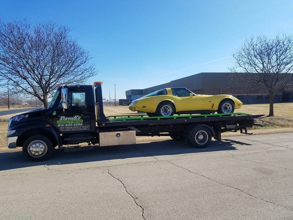 Black tow truck carrying a yellow sports car on a sunny day.