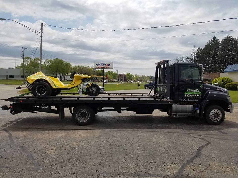 A yellow three-wheeled vehicle is loaded on the flatbed of a black tow truck.