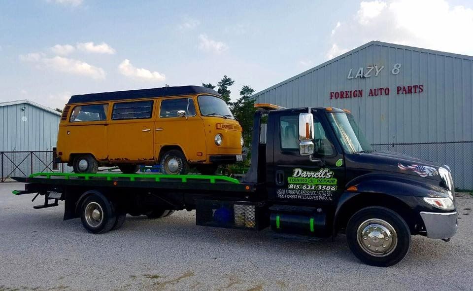Yellow VW van loaded on a black tow truck in front of a building labeled 