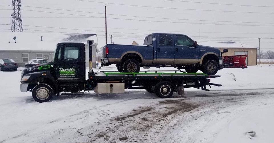 Tow truck carrying a blue pickup truck on a snow-covered road.