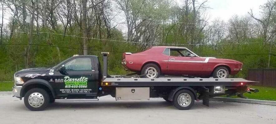 A red vintage car on a tow truck. The truck is black with green lettering.