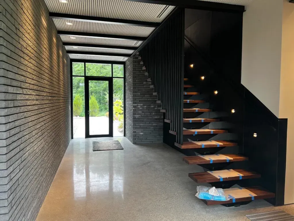 Hallway with brick wall, floating stairs, and a door leading outside.