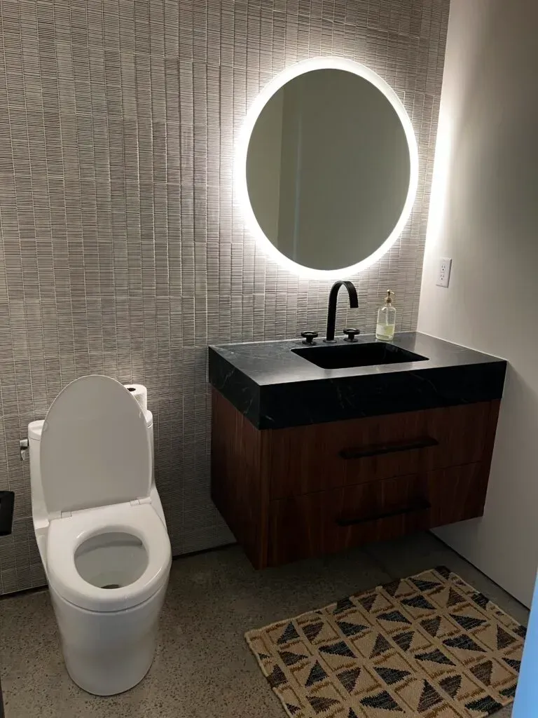 Modern bathroom with a toilet, floating vanity, circular mirror, and patterned rug.