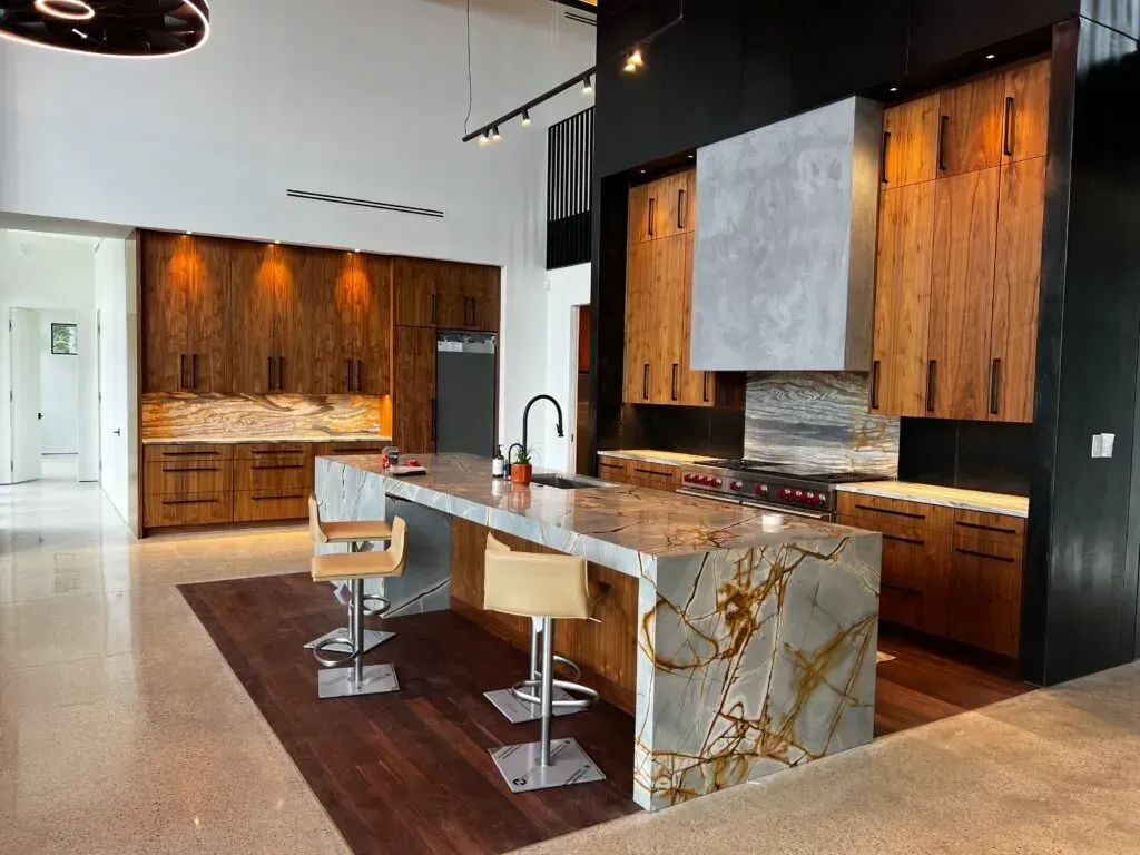 Modern kitchen with wood cabinets, stone island, stainless steel appliances, and concrete floors.