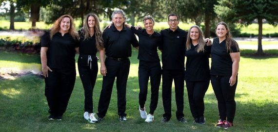 A group of seven people standing in a grassy area, all wearing black clothing, posing for a photo.