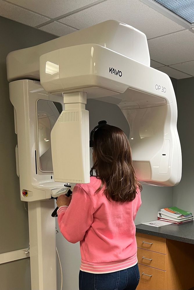 Woman receiving a dental panoramic x-ray. White machine, pink shirt, dental office setting.