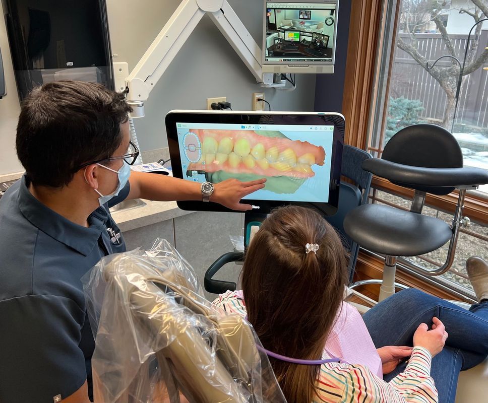 Dentist pointing at a 3D teeth scan on a screen, explaining it to a patient in a dental office.