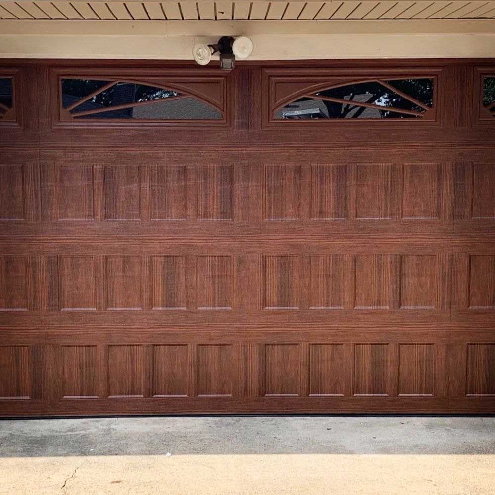 Dark brown garage door with decorative panels, windows, and light fixture.