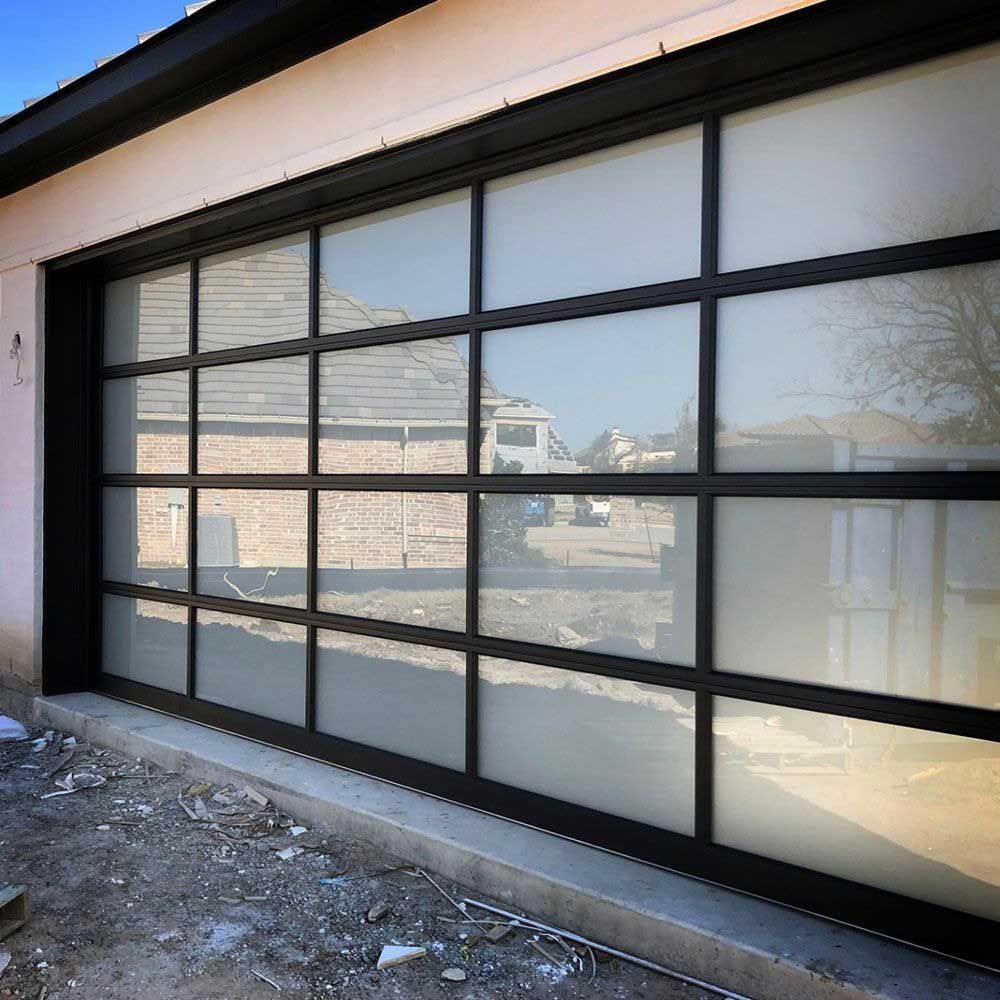 Black-framed garage door with frosted glass panes, reflecting the exterior scene; set in a light-colored building.