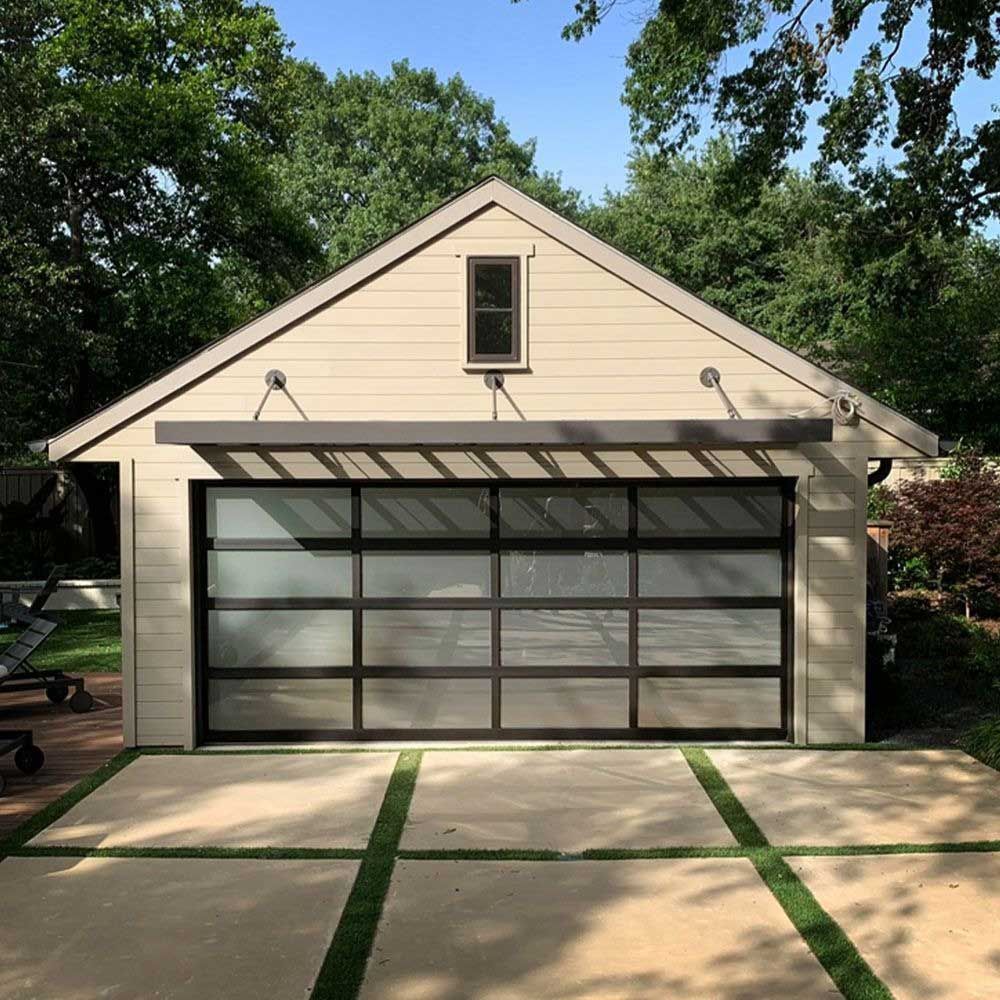 Beige garage with glass door, concrete driveway with green grass squares, trees in background.