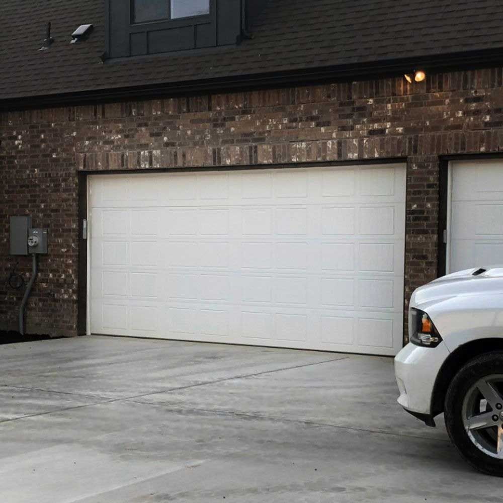 White garage door on brick building, with a white car parked in the driveway.