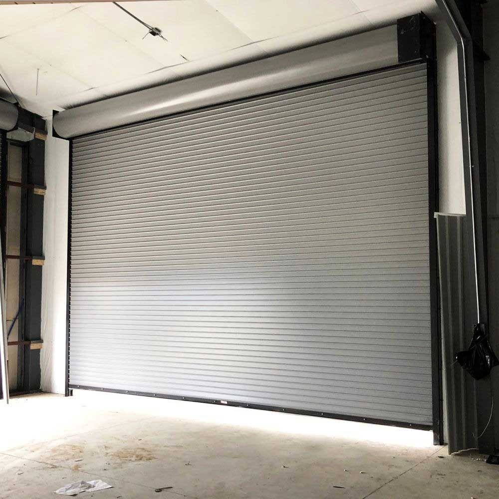 Gray metal roll-up garage door, closed, inside a warehouse.